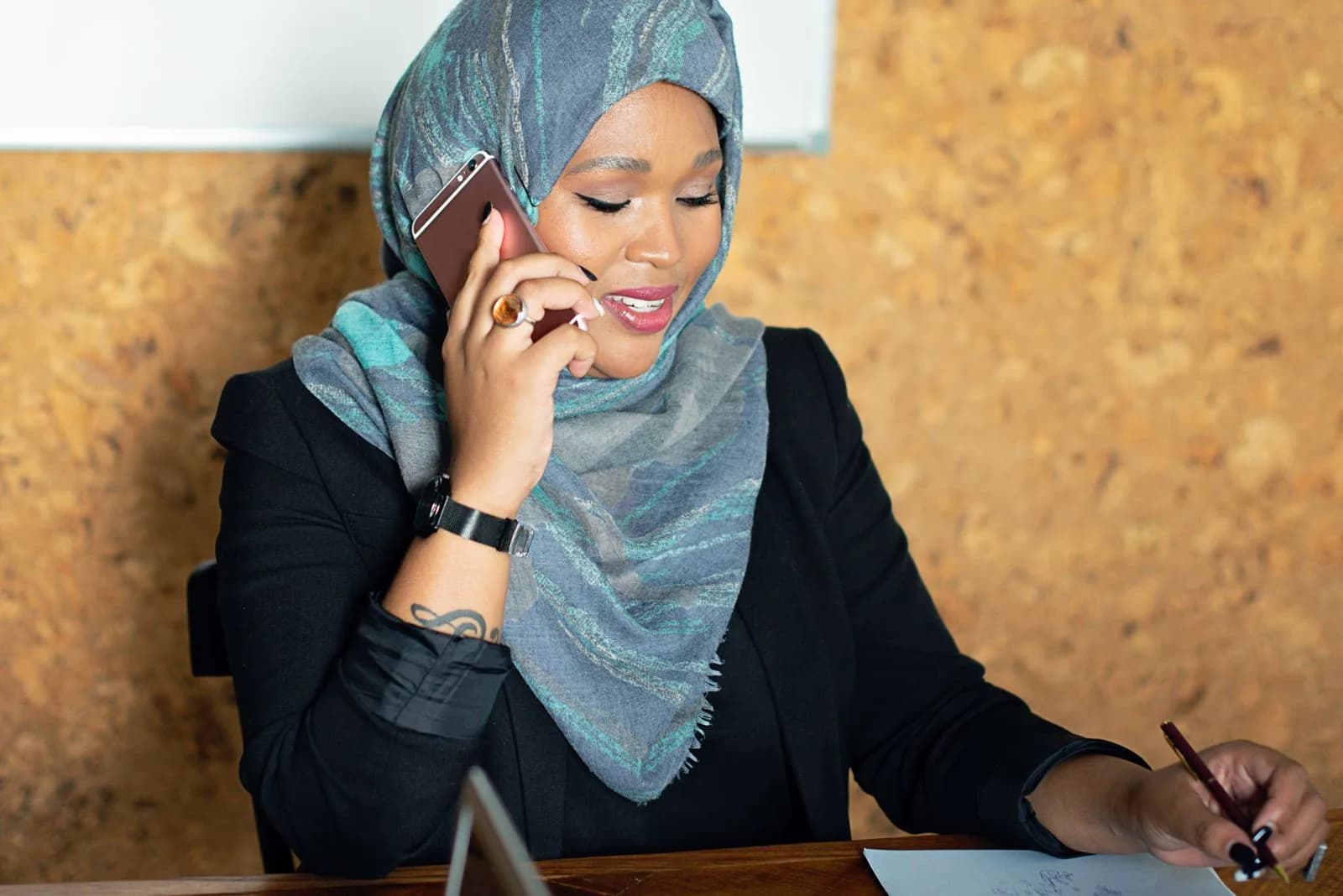 A person writes notes while talking on a smartphone.