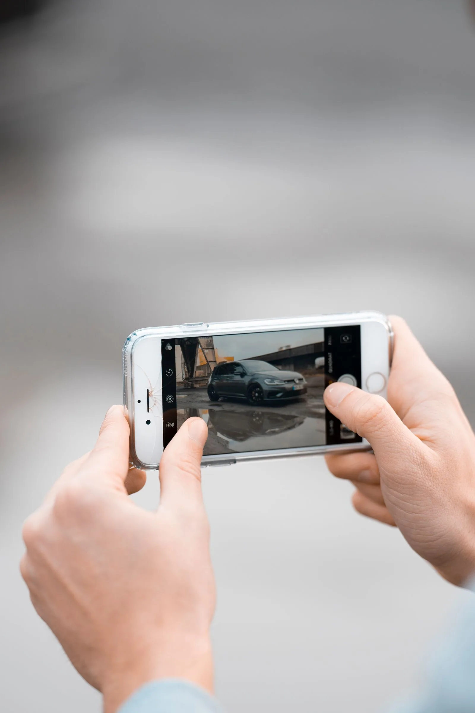 Hands using a smartphone to photograph a parked car.